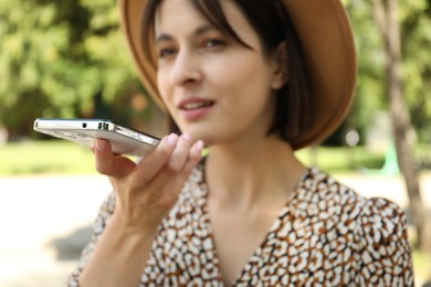 Photo of Beautiful woman recording voice message via smartphone outdoors, selective focus