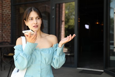 Photo of Beautiful woman recording voice message via smartphone outdoors