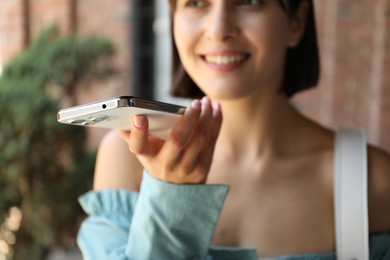 Photo of Beautiful woman recording voice message via smartphone outdoors, selective focus