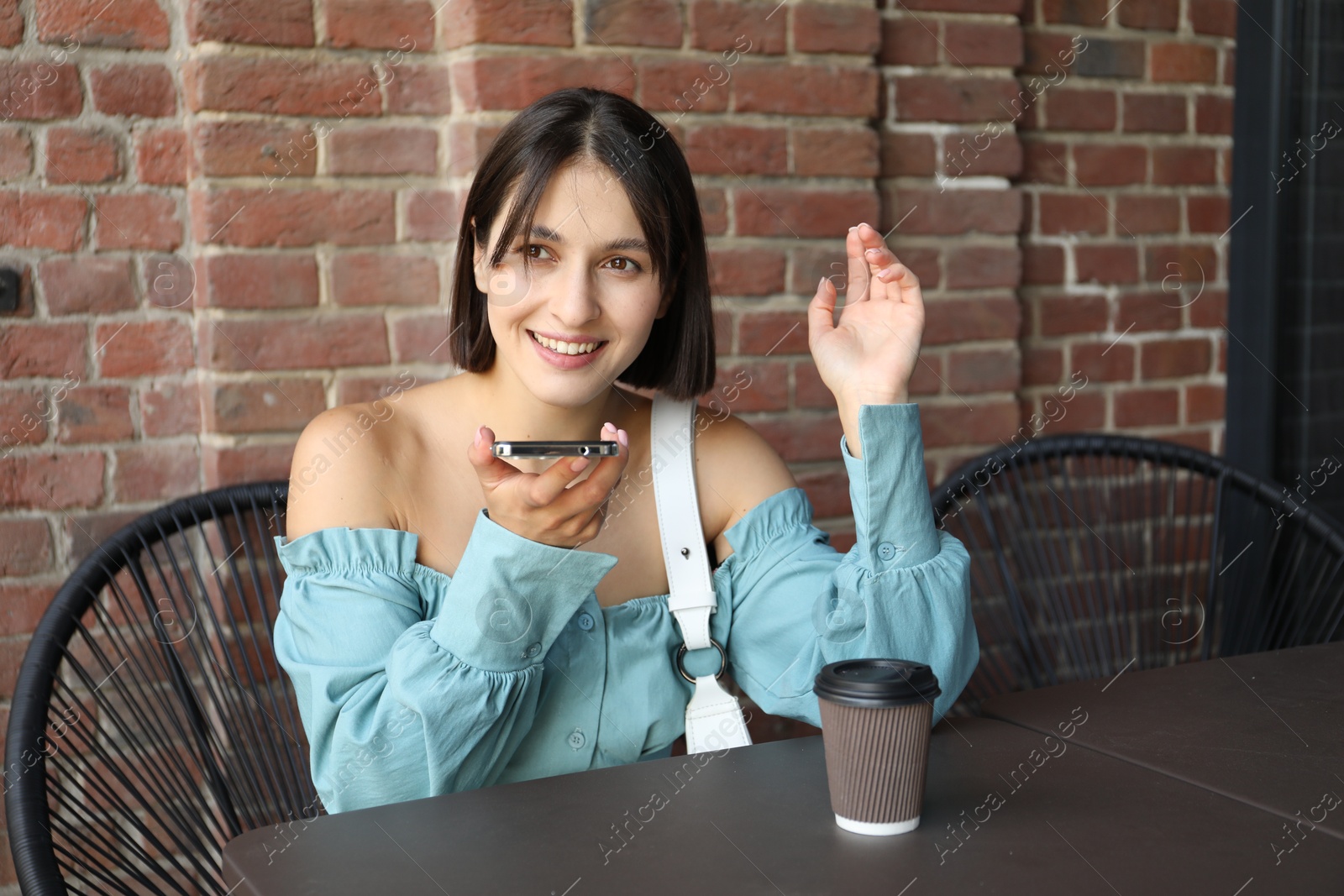 Photo of Beautiful woman recording voice message via smartphone in outdoors cafe