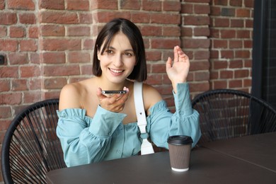 Photo of Beautiful woman recording voice message via smartphone in outdoors cafe