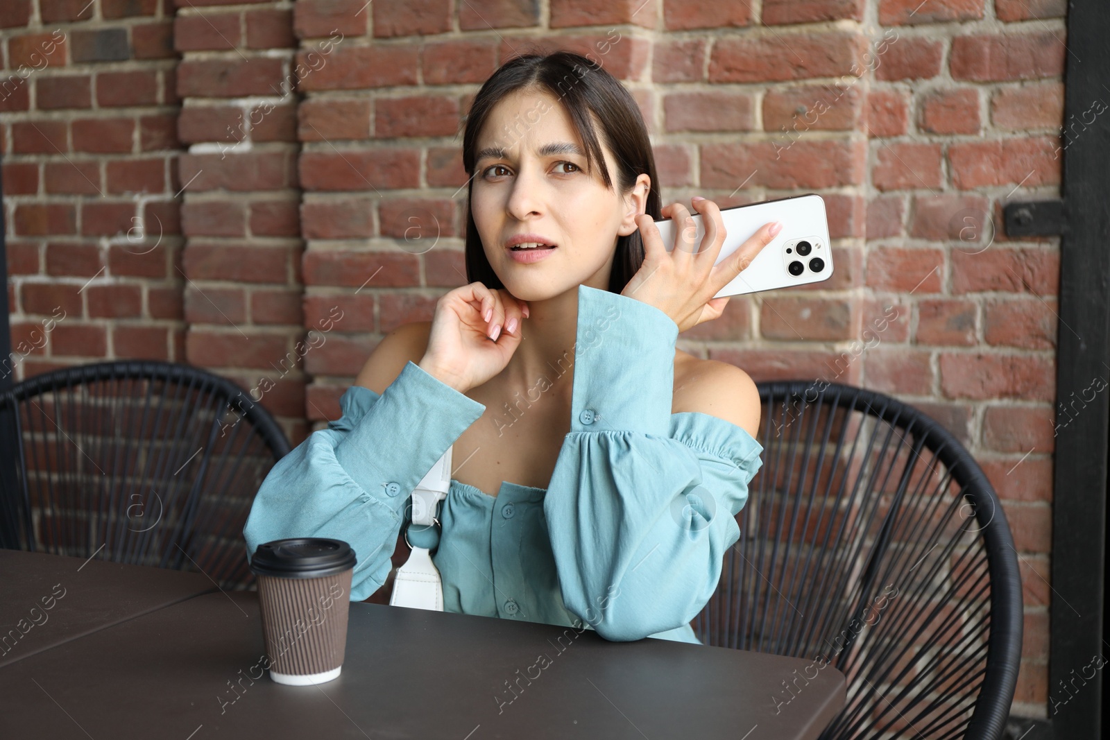 Photo of Beautiful woman with smartphone listening to voice message in outdoor cafe