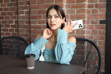 Photo of Beautiful woman with smartphone listening to voice message in outdoor cafe