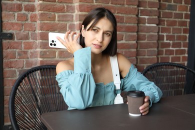 Beautiful woman with smartphone listening to voice message in outdoor cafe