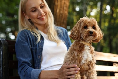 Beautiful young woman with cute dog on bench in park, selective focus