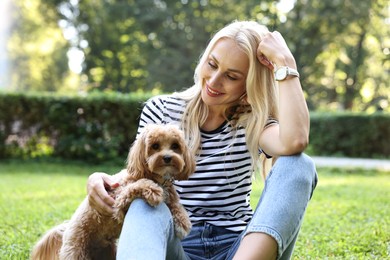 Beautiful young woman with cute dog on green grass in park