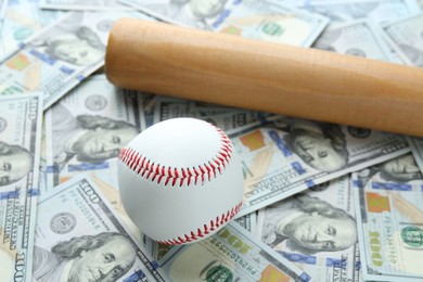 Photo of Baseball ball and bat on dollars bills, closeup