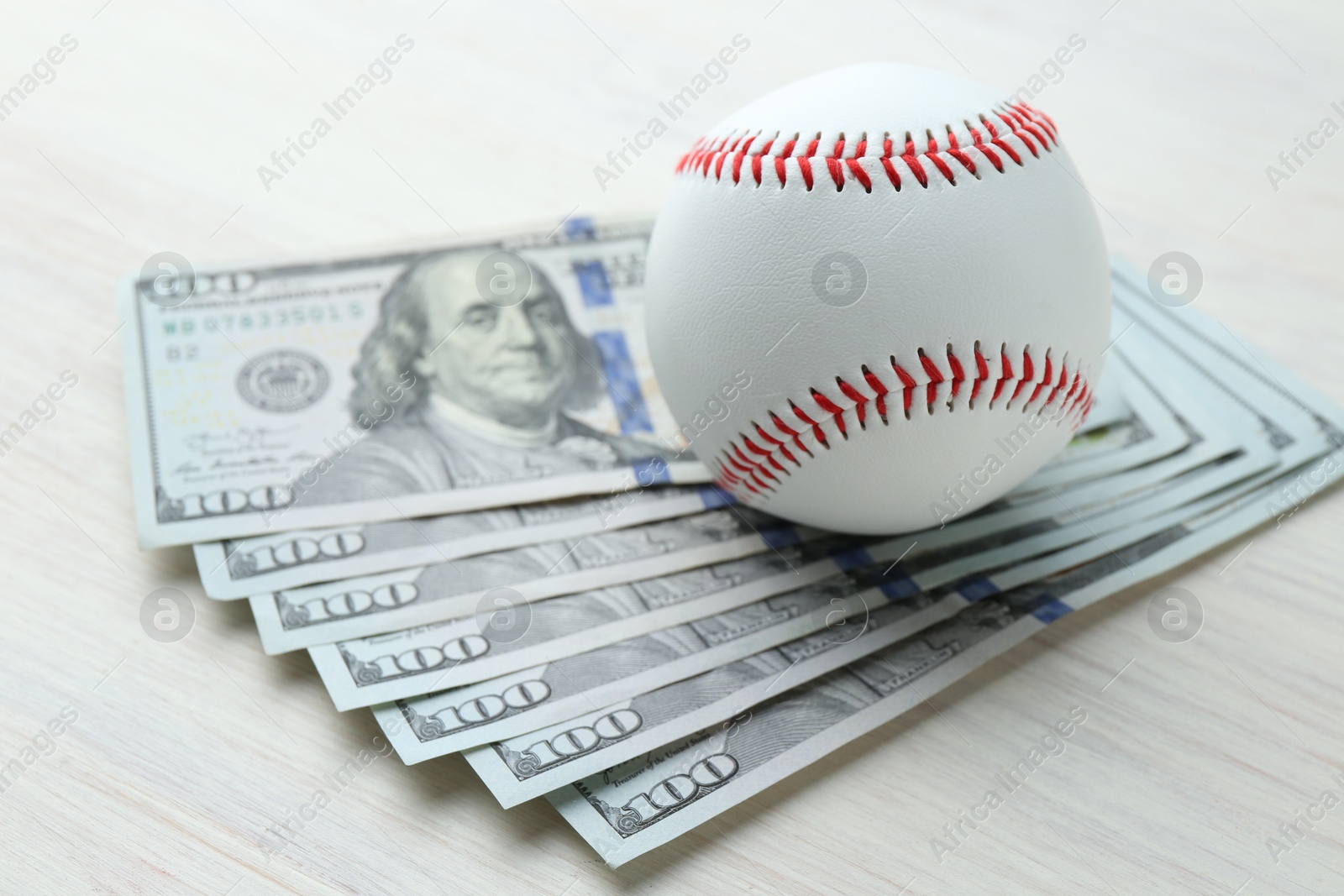 Photo of Baseball ball and dollar bills on white wooden table, closeup