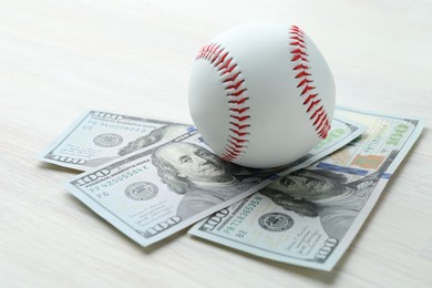 Photo of Baseball ball and dollar bills on white wooden table, closeup