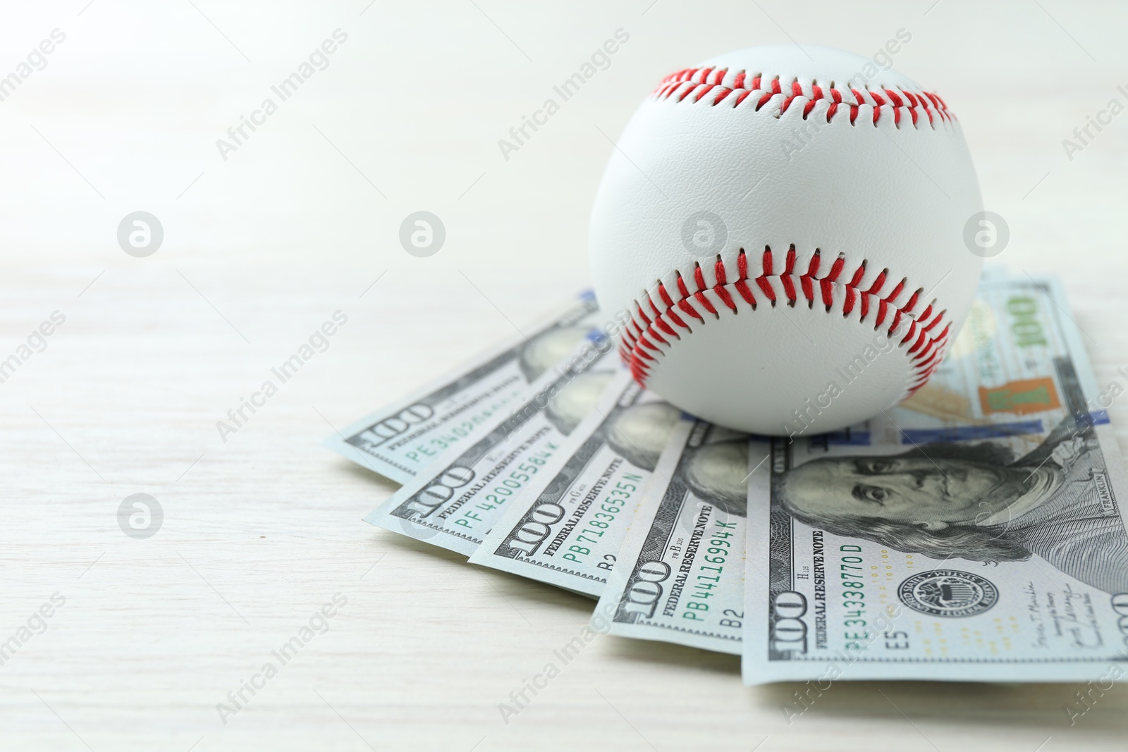 Photo of Baseball ball and dollar bills on white wooden table, closeup. Space for text