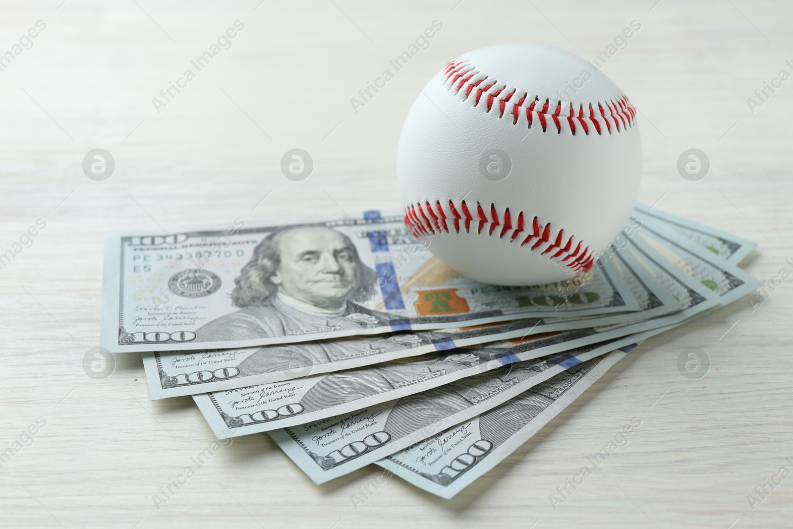 Photo of Baseball ball and dollar bills on white wooden table, closeup