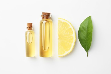 Photo of Bottles of essential oils, lemon and green leaf on white background, flat lay