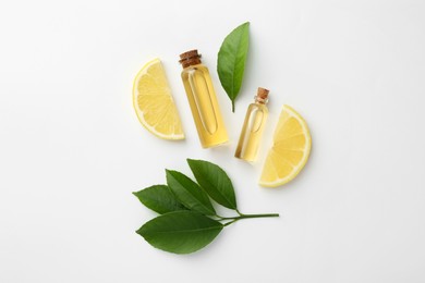 Bottles of essential oils, lemon and green leaves on white background, flat lay