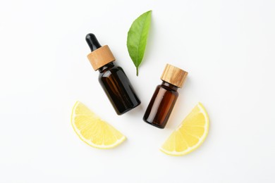 Photo of Bottles of essential oils, lemon and green leaf on white background, flat lay