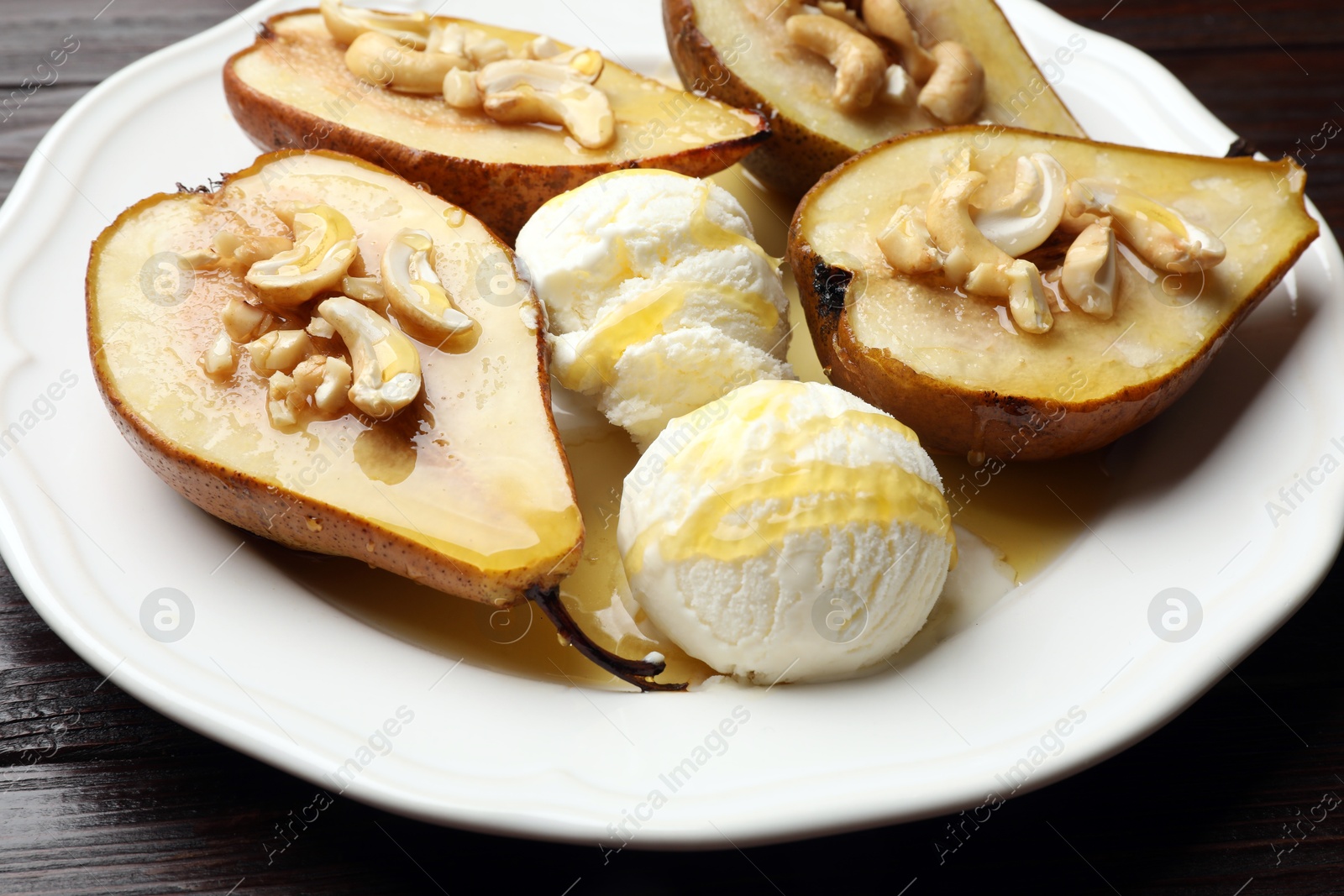 Photo of Delicious baked pears with nuts, ice cream and honey on wooden table, closeup