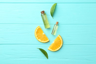 Bottles of essential oils, orange and green leaves on turquoise wooden table, flat lay