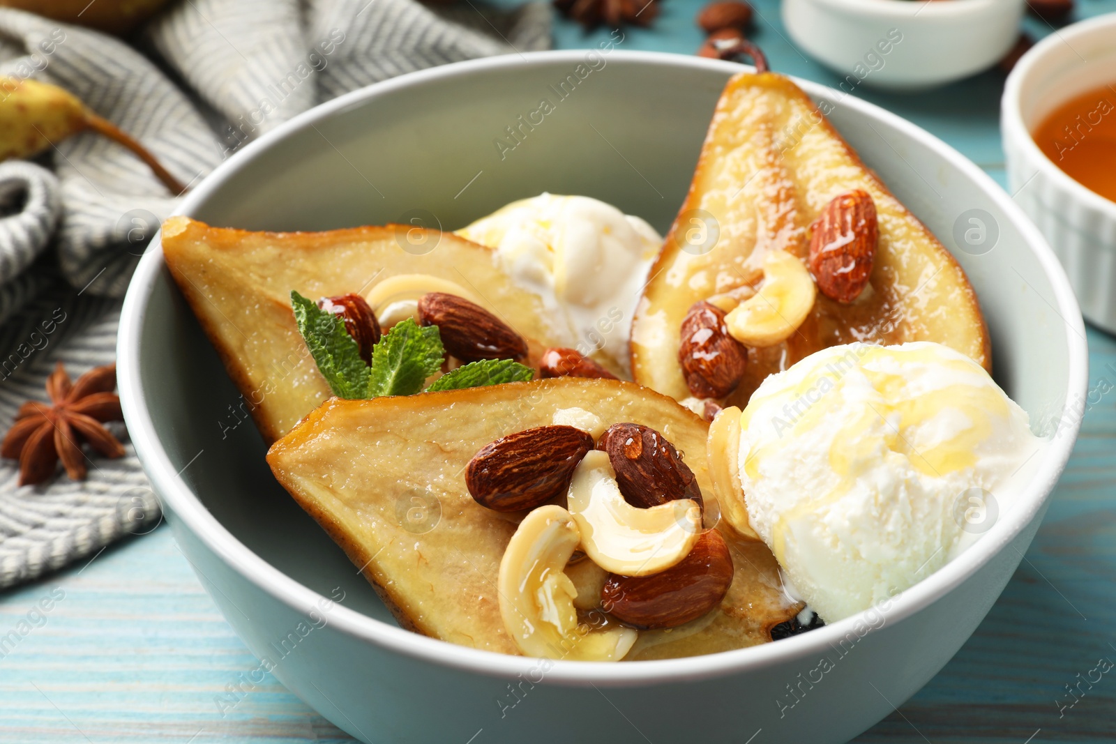 Photo of Delicious baked pears with nuts, ice cream and honey in bowl on light blue wooden table, closeup