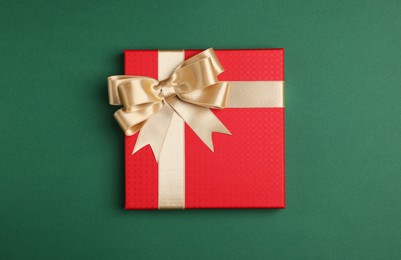 Photo of Beautiful red gift box with bow on green background, top view