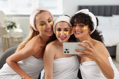 Happy friends with eye patches taking selfie indoors. Spa party