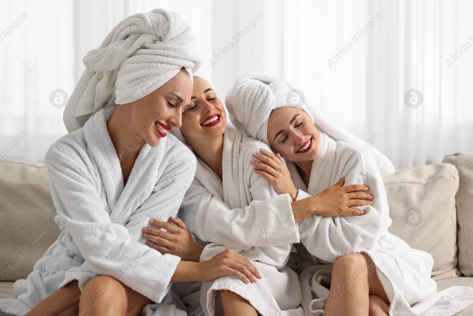 Photo of Happy friends in bathrobes with towels on couch indoors. Spa party