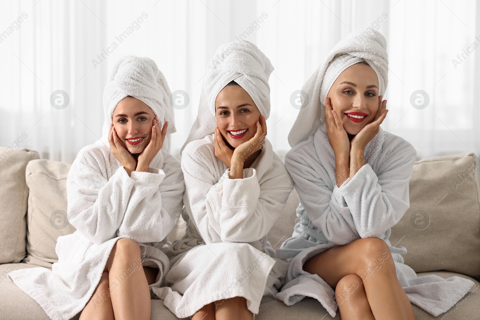 Photo of Happy friends in bathrobes with towels on couch indoors. Spa party