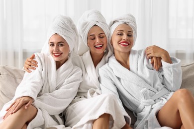 Happy friends in bathrobes with towels on couch indoors. Spa party