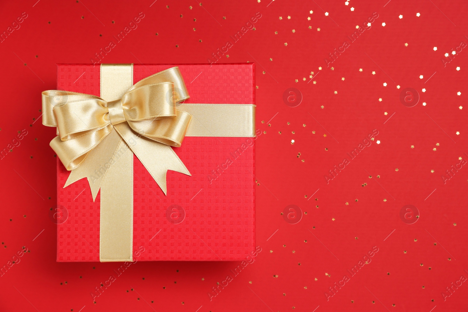 Photo of Gift box with bow and confetti on red background, top view. Space for text