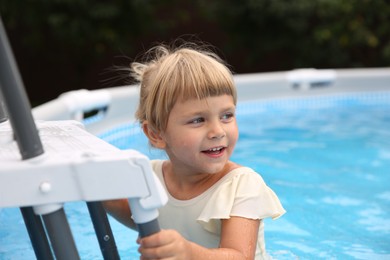 Little girl getting out of swimming pool by ladder outdoors