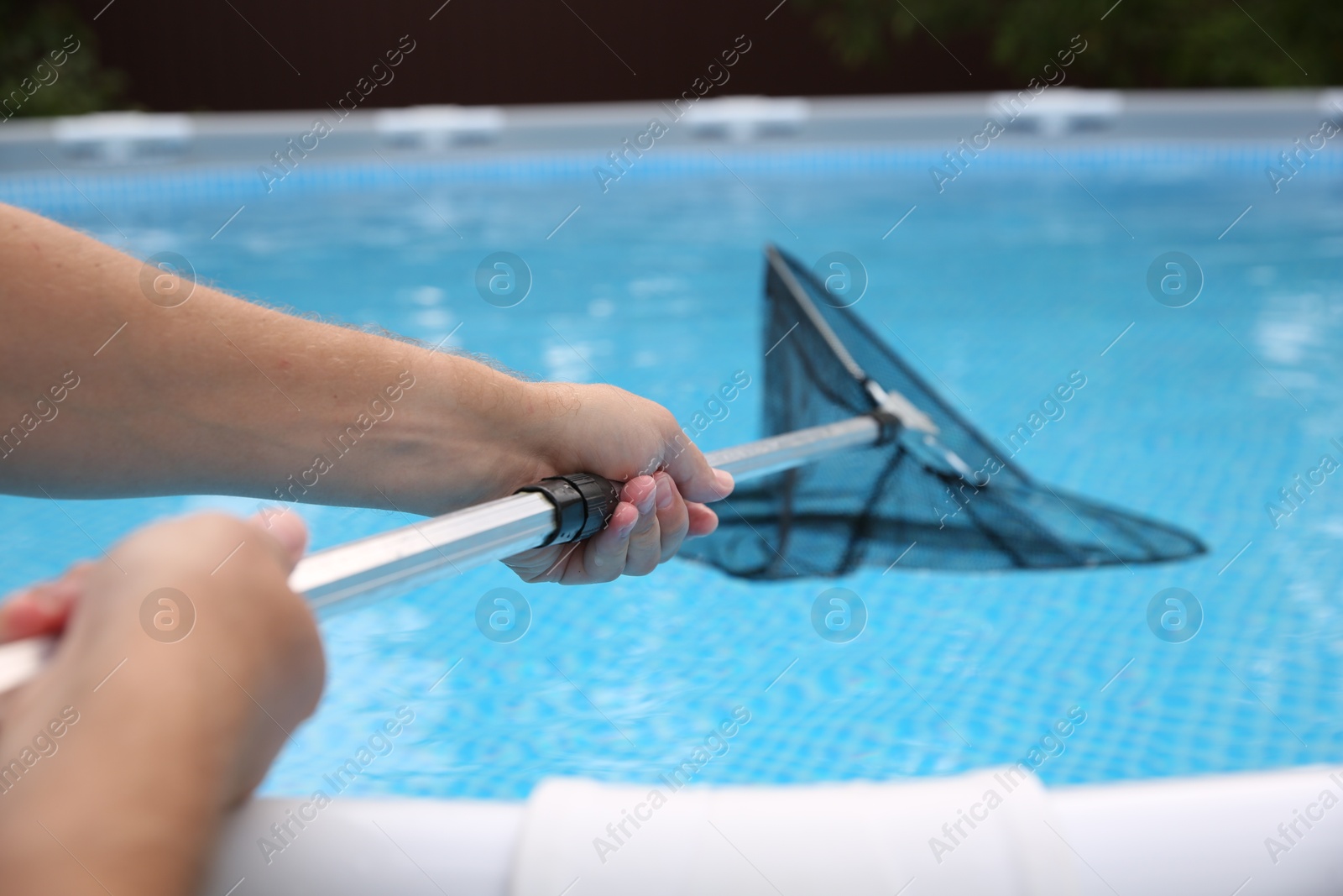 Photo of Man cleaning swimming pool with skimmer net, closeup