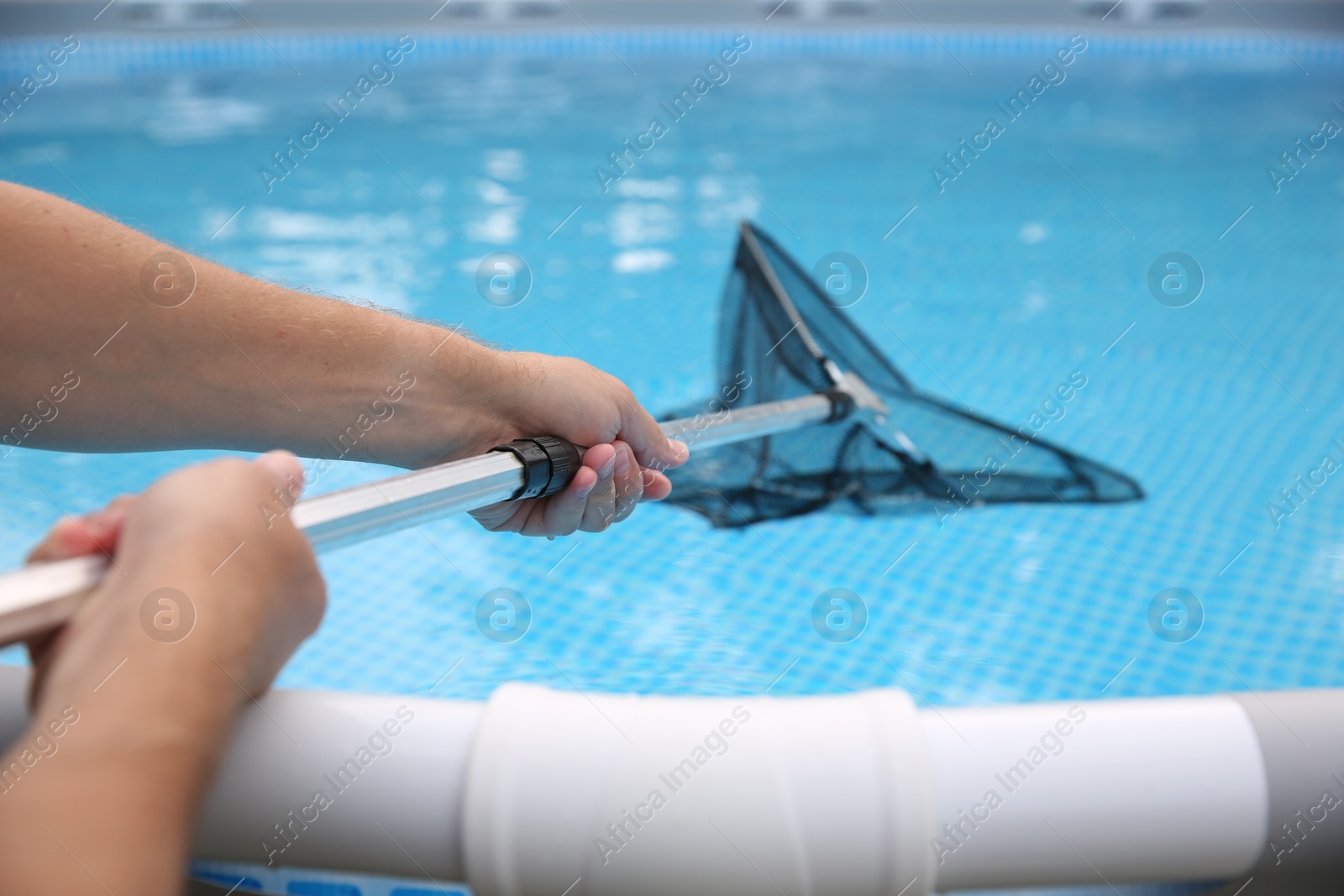 Photo of Man cleaning swimming pool with skimmer net, closeup