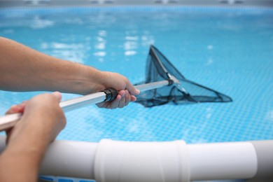 Photo of Man cleaning swimming pool with skimmer net, closeup