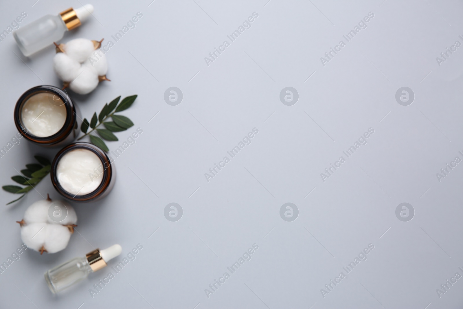 Photo of Different cosmetic products, leaves and cotton flowers on grey background, flat lay. Space for text