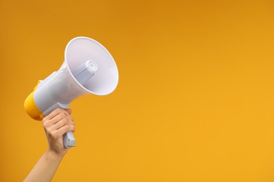 Photo of Woman holding megaphone speaker on orange background, closeup. Space for text