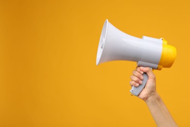 Woman holding megaphone speaker on orange background, closeup. Space for text