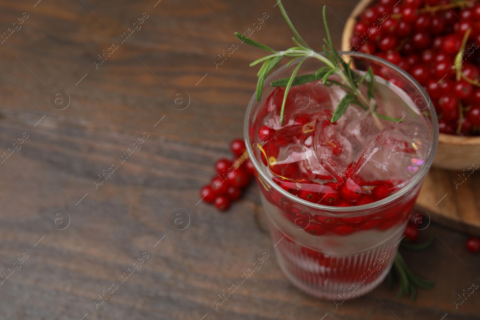 Photo of Refreshing water with red currants and rosemary in glass on wooden table, closeup. Space for text