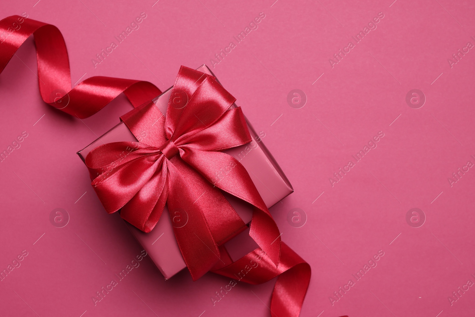 Photo of Gift box with bow on pink background, top view. Space for text