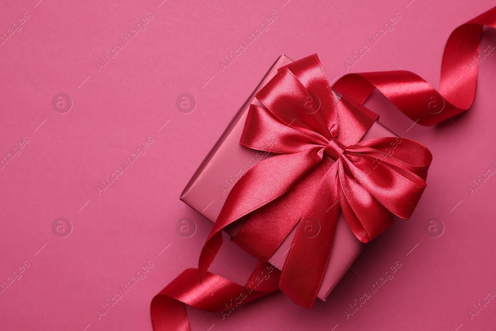 Photo of Gift box with bow on pink background, top view. Space for text