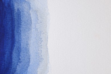 Blue watercolor painting on white paper, top view. Space for text