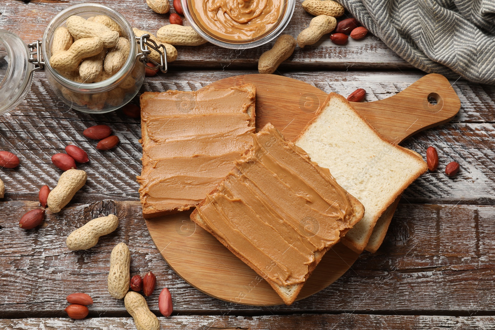 Photo of Delicious sandwiches with peanut butter and fresh nuts on wooden table, flat lay