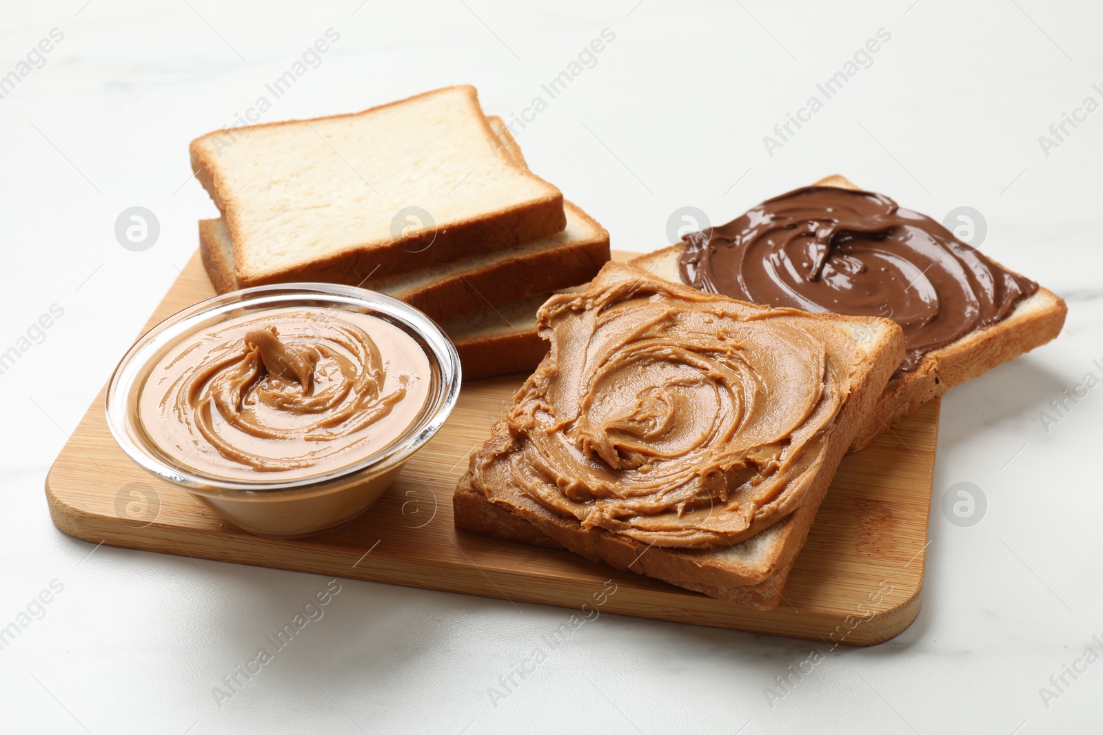 Photo of Delicious sandwiches with peanut butter and chocolate paste on white table, closeup