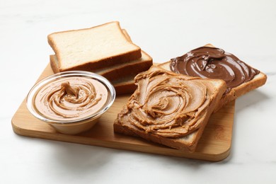 Photo of Delicious sandwiches with peanut butter and chocolate paste on white table, closeup