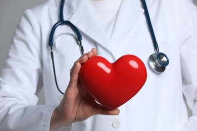 Doctor with red heart on grey background, closeup