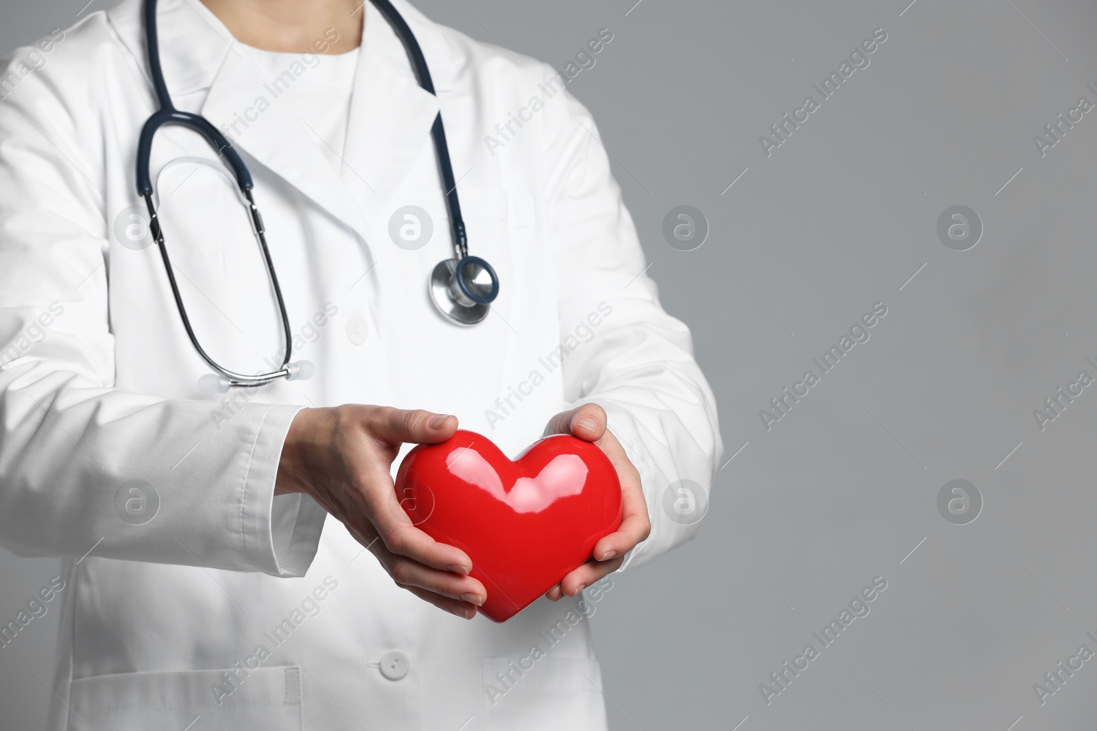 Photo of Doctor with red heart on grey background, closeup. Space for text