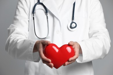 Doctor with red heart on grey background, closeup