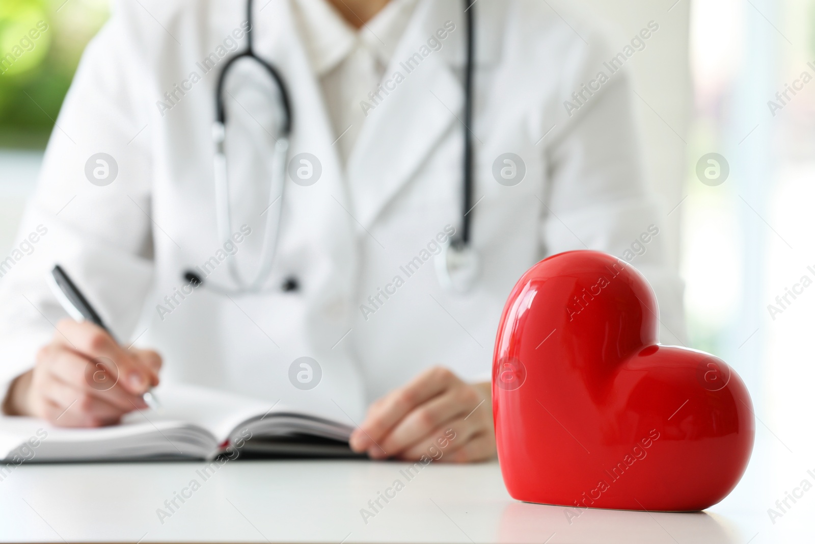 Photo of Doctor working at table in clinic, focus on red heart