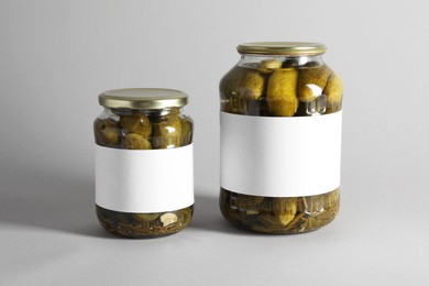 Pickled cucumbers in jars on light background