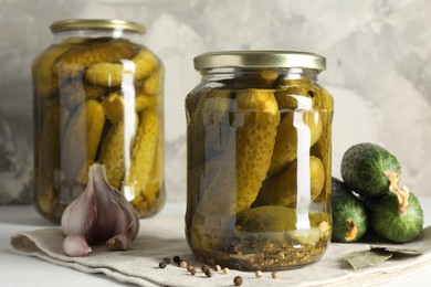 Pickles in jars, fresh cucumbers and spices on white table