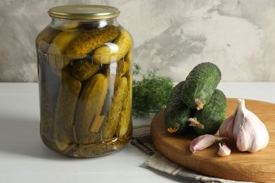 Photo of Pickles in jar, fresh cucumbers, garlic and dill on white table