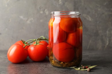 Tasty pickled tomatoes in jar, bay leaves, peppercorns and fresh vegetables on grey table