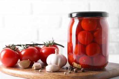 Tasty pickled tomatoes in jar, fresh vegetables and spices on white table